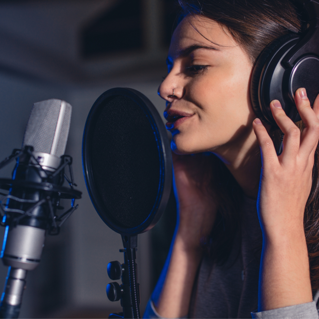 Eine Kopfhörer tragende Frau singt lächelnd in ein Mikrofon