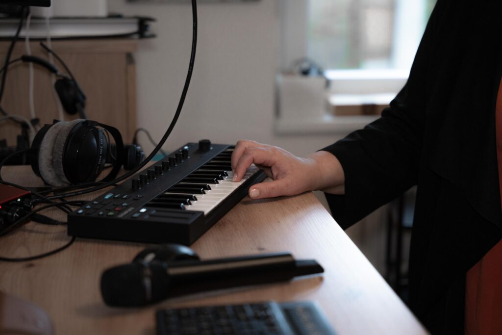 Eine Hand spielt auf einem Midi-Keyboard, daneben liegt ein Mikrofon